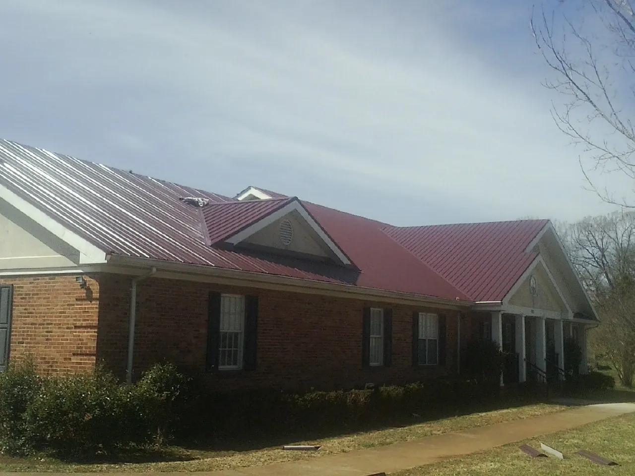 Red metal roof with gabled entries on a long brick building, from a Hail Damage Roof Repair job in Doylestown